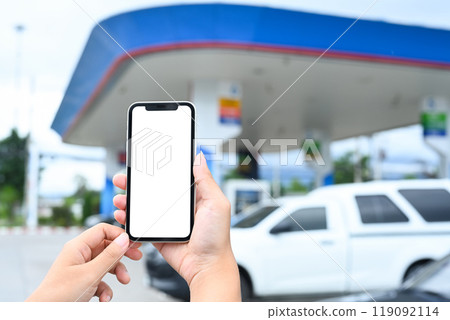 Close up shot of woman holding smartphone with blank screen on the background of a gas station 119092114