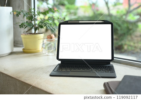 Digital tablet with blank screen on a table next to a potted plant and notebooks Digital tablet with blank screen on a table next to a potted plant and notebooks 119092117