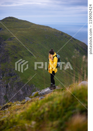 A Solo Female Hiker in a Bright Yellow Jacket Walking Along a Scenic Mountain Pathway A Solo Female Hiker in a Bright Yellow Jacket Walking Along a Scenic Mountain Pathway 119092424