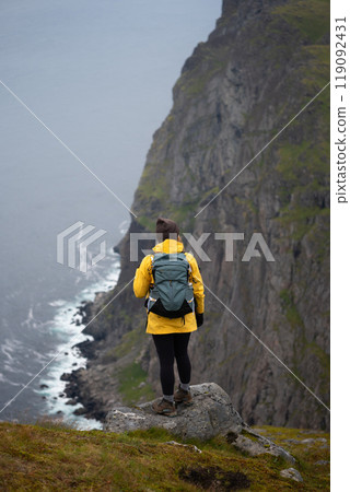 An adventurous female stands at a cliffs edge, surrounded by a stunning, misty landscape. An adventurous female stands at a cliffs edge, surrounded by a stunning, misty landscape. 119092431