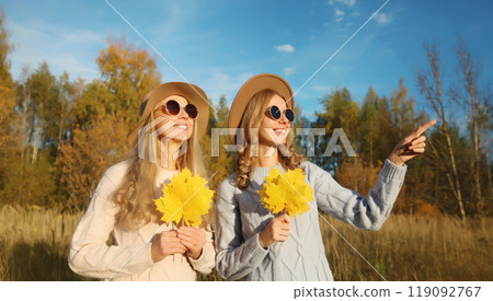 Happy young two women friends with autumn yellow leaves, stylish girlfriends smiles together in park 119092767