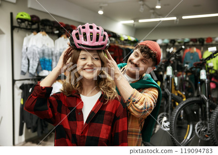 Cheerful man and woman couple wearing bicyclist helmet choosing safety gear Cheerful man and woman couple wearing bicyclist helmet choosing safety gear 119094783