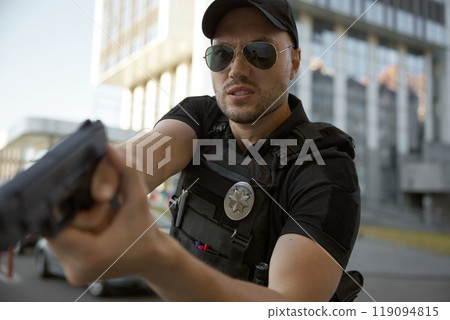 Portrait of man patrol police officer aiming with handgun at city street Portrait of man patrol police officer aiming with handgun at city street 119094815
