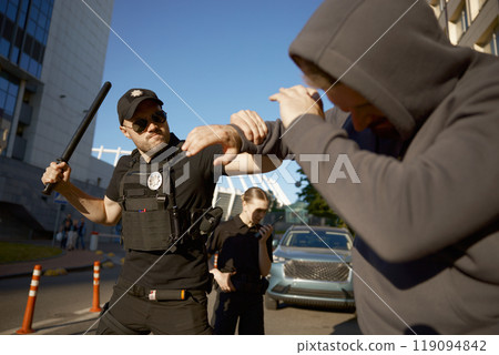 Policeman with baton attacking aggressive male offender to arrest 119094842