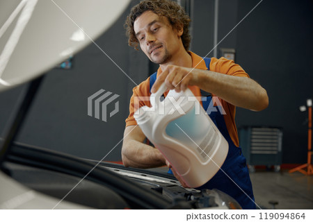 Man auto mechanic pouring mineral motor oil in car engine 119094864