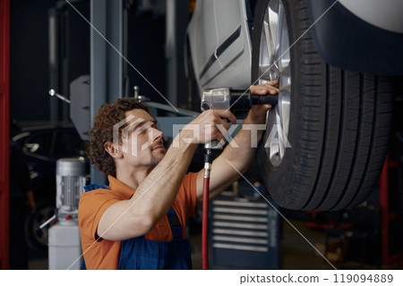 Male auto mechanic using impact wrench during tires replacement 119094889