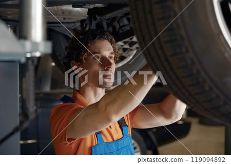 Professional mechanic repairing wheel fixing problem standing under car Professional mechanic repairing wheel fixing problem standing under car 119094892