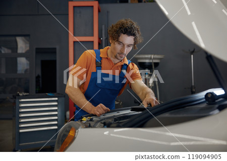 Male mechanic looking under car hood checking engine operation work 119094905
