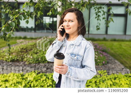 Woman Enjoying Coffee Outdoors Talking on Phone in Urban Green Space. Woman Enjoying Coffee Outdoors Talking on Phone in Urban Green Space. 119095200