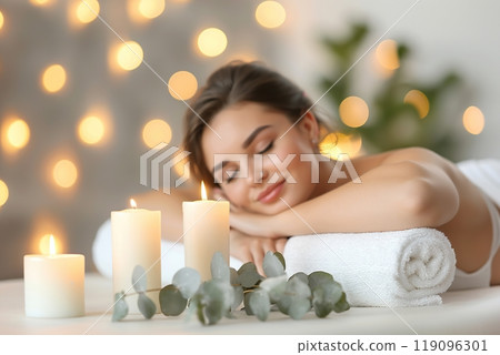 Young woman enjoying exotic massage. Relaxed girl lying on a bed. Spa items for procedures on the foreground. Candles, essential oils and sea salt. Aromatherapy. Beauty treatment and relax concept. Young woman enjoying exotic massage. Relaxed girl lying on a bed. Spa items for procedures on the foreground. Candles, essential oils and sea salt. Aromatherapy. Beauty treatment and relax concept. 119096301