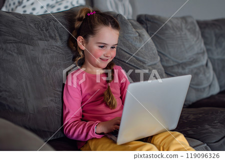 Little girl using laptop sitting sofa. Cute little girl using technology device sitting at home alone. Girl playing on phone. One person. Happy elementary age kid rest on couch enjoy weekend Little girl using laptop sitting sofa. Cute little girl using technology device sitting at home alone. Girl playing on phone. One person. Happy elementary age kid rest on couch enjoy weekend 119096326