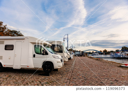 Scenic view many campers motorhome parked at camping site at Elbe river embankment Passenger trip cruise ship docked morning sunrise sky. Motorhome station travel destination. RV lifestyle Scenic view many campers motorhome parked at camping site at Elbe river embankment Passenger trip cruise ship docked morning sunrise sky. Motorhome station travel destination. RV lifestyle 119096373