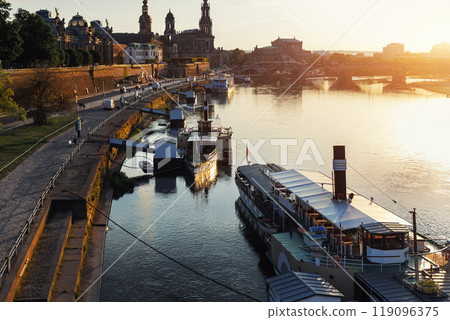 Scenic warm sunset beautiful Dresden city skyline at Elbe River with many steam tourist ship vessel moored at bank. Saxony Germany capital cityscape dusk panoramic view with old Europe architecture 119096375