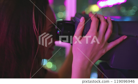 Woman on a rooftop at night, using binoculars to observe the vibrant city lights below, filled with wonder and excitement Woman on a rooftop at night, using binoculars to observe the vibrant city lights below, filled with wonder and excitement 119096946