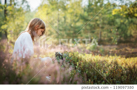 A young child sits peacefully among wildflowers in a serene forest during a bright summer afternoon A young child sits peacefully among wildflowers in a serene forest during a bright summer afternoon 119097380