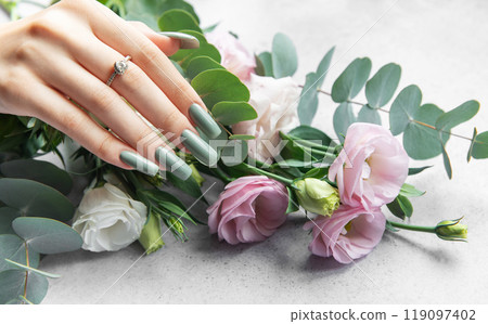 Elegant hand adorned with a ring showcasing stylish green nails beside a bouquet Elegant hand adorned with a ring showcasing stylish green nails beside a bouquet 119097402