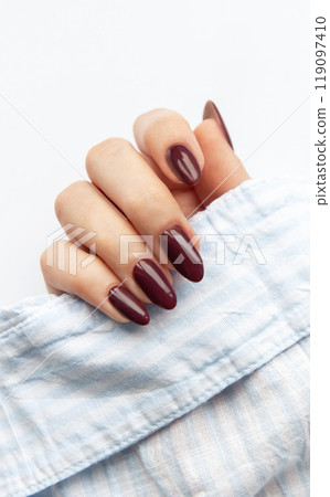 Elegant dark red manicure displayed on a womans hand with a soft blue fabric background  119097410