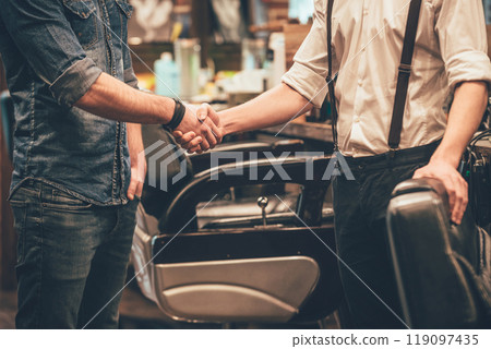 Handshake at barbershop. Close-up of barber and his client shaking hands while standing at barbershop 119097435