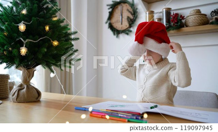 A boy in a red New Year's cap. A little boy puts on a New Year's cap in a Christmas atmosphere in the interior. 119097945