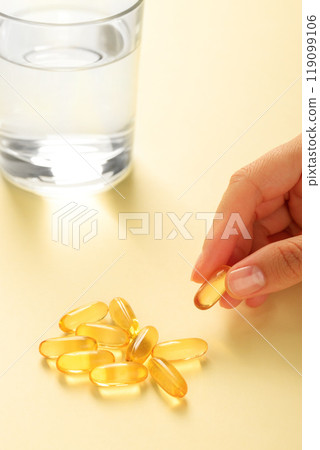 Hand picks up one omega-3 capsule from a handful of similar capsules. Hand picks up one omega-3 capsule from a handful of similar capsules. 119099106