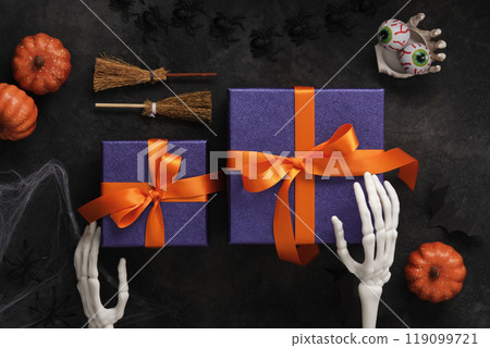 Purple Halloween gift boxes with orange ribbons with skeleton hands, broomstick, pumpkins and spooky decorations Purple Halloween gift boxes with orange ribbons with skeleton hands, broomstick, pumpkins and spooky decorations 119099721