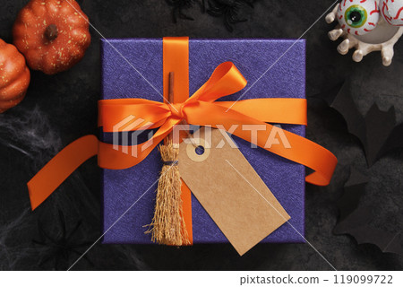 Purple Halloween gift box with orange ribbon, blank label and broom. Space for your text 119099722