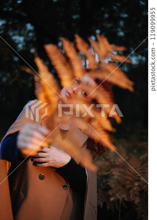 Young woman hiding behind fern leaf in dark forest Young woman hiding behind fern leaf in dark forest 119099955