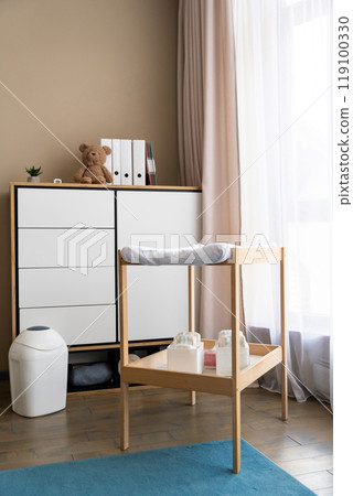 Empty nursery with changing table with diapers, lamp, commode and window with simple curtains Empty nursery with changing table with diapers, lamp, commode and window with simple curtains 119100330