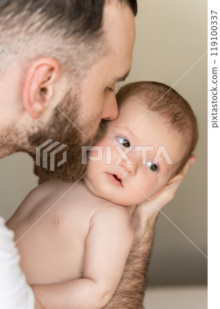 Bearded man young father kissing newborn baby girl or boy in home interior 119100337