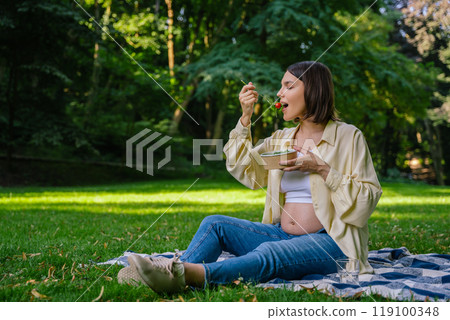 Pretty pregnant young woman eating lunch in the park Pretty pregnant young woman eating lunch in the park 119100348