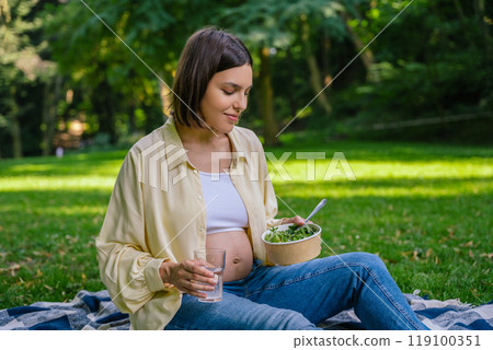Pretty pregnant young woman eating lunch in the park 119100351