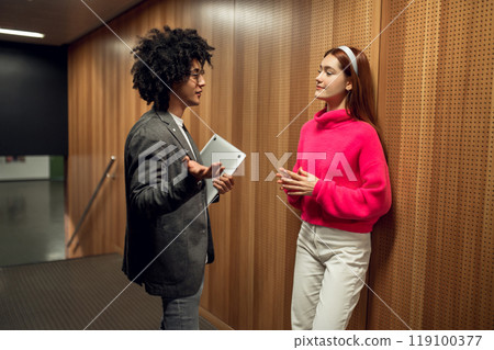 Two young people talking in the corridor and looking involved 119100377
