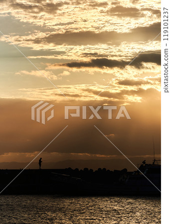 Silhouettes of fishing boats and fishermen floating in the harbor at dusk 119101237