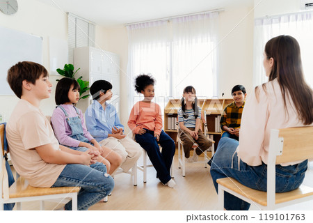 Group study session with diverse students seated in a circle engaging in a classroom discussion led by a teacher, emphasizing interactive learning and participation in a primary education environment Group study session with diverse students seated in a circle engaging in a classroom discussion led by a teacher, emphasizing interactive learning and participation in a primary education environment 119101763