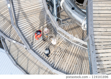 People navigate the winding wooden pathway of the Sky Walk Tower in Swieradow Zdroj, enjoying panoramic views of the picturesque Jizera Mountains on a sunny day. 119101896
