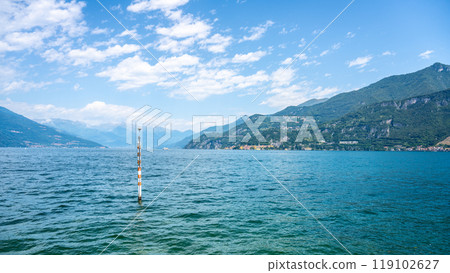 Gentle ripples form on Lake Como's surface as a serene atmosphere envelops the landscape. The mountains stand tall in the background, showcasing the beauty of this Italian gem. 119102627