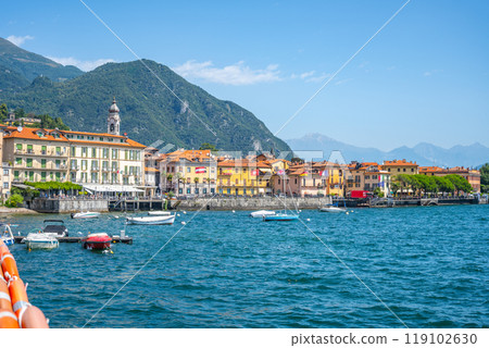 Menaggio nestled by Lake Como showcases colorful buildings and boats gently bobbing in the water, capturing the essence of Italian lakeside charm on a bright sunny day. 119102630