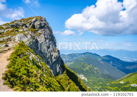 A breathtaking view from a rocky mountain trail in Low Tatras National Park, Slovakia. Lush greenery surrounds the path, offering stunning vistas of distant peaks and valleys. 119102701