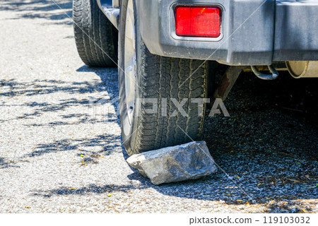 Stone under the car wheel, parking on slope, secure from roll away, safety concept Stone under the car wheel, parking on slope, secure from roll away, safety concept 119103032
