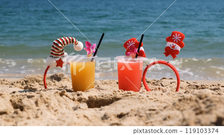 Vibrant fruit cocktails with Christmas decorations rest on warm sand by the sea, celebrating winter holidays in the tropics 119103374