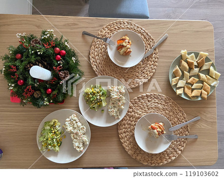 Festive dining table set with an assortment of homemade dishes, complemented by a decorative holiday wreath centerpiece. Warmth and joy of gathering for a shared meal during holiday season 119103602