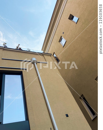 Looking up at the intersection of two modern beige buildings against a bright blue sky. Minimalist urban scene, highlighting the contrast between architecture and open sky 119103658