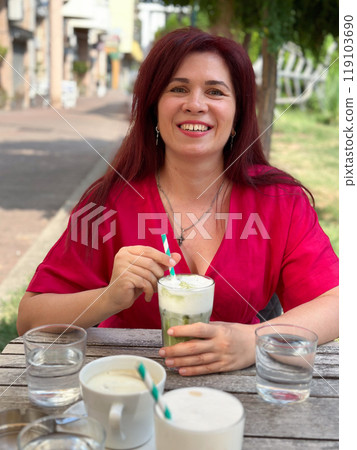 Woman enjoying a refreshing drink at an outdoor cafe in a vibrant setting. Relaxation and the joy of savoring a leisurely afternoon 119103690