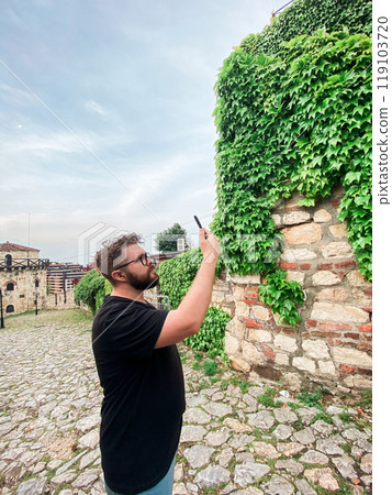 A man takes a photo while standing at a viewpoint in fortress. A tourist with a smartphone camera 119103720