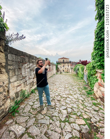 A man takes a photo while standing at a viewpoint in fortress. A tourist with a smartphone camera 119103723