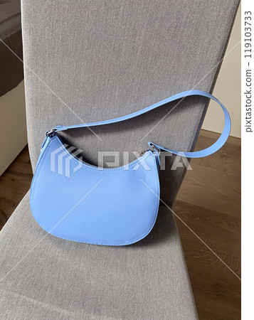 Blue mini bag standing on chair indoors, style element, trendy wardrobe detail of stylish woman. Front view. Blue mini bag standing on chair indoors, style element, trendy wardrobe detail of stylish woman. Front view. 119103733