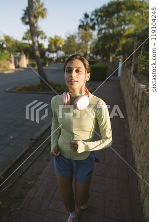 A Young Woman is Jogging Outdoors in the Glorious Early Morning Sunlight with Energy 119104248