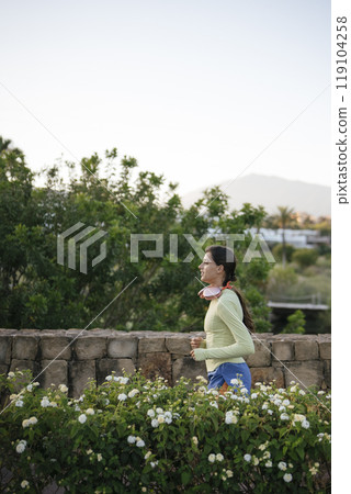A young woman jogging enthusiastically in a beautiful natural setting with a scenic backdrop A young woman jogging enthusiastically in a beautiful natural setting with a scenic backdrop 119104258