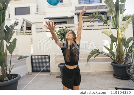 A young woman happily playing with a ball in a sunny outdoor setting, full of joy and energy A young woman happily playing with a ball in a sunny outdoor setting, full of joy and energy 119104320