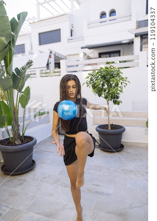 A Graceful Woman Skillfully Balancing a Ball in a Modern Outdoor Setting with Elegance 119104337